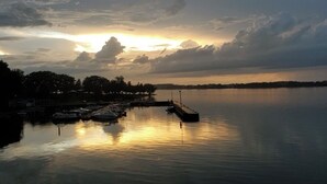 Marina con barcos amarrados, agua tranquila y un atardecer de fondo.