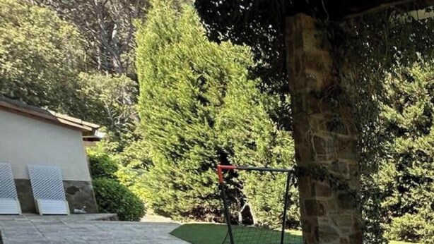 Un patio al aire libre con mobiliario de mimbre, una mesa redonda y un muro de piedra.