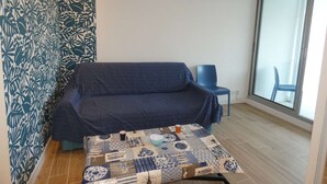 Una stanza con una parete decorata, un divano, una poltrona, un tavolo con una coperta e un'ampia finestra.