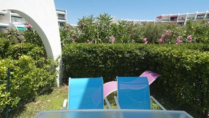 Una vista di un cortile alberghiero con due poltrone blu, un edificio bianco e un siepe fiorita di rosa.