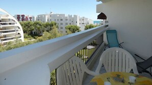 A balcony with white chairs and a table, overlooking a residential area with white buildings and greenery. - Charming Studio by Beach with Private Parking and Garden Views (La Grande-Motte)