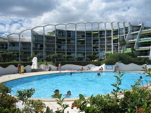 A swimming pool surrounded by a modern building with multiple balconies and a clear sky. - Charming 2-Room Apartment with Pool, Near Beach, Sleeps 5 (La Grande-Motte)