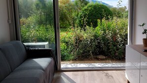 Ein Zimmer mit einer Couch, einem Tisch und Blick auf einen Garten durch eine Schiebetür.