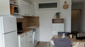 Eine kleine Küche mit weißen Schränken, einem eingebauten Backofen, einer Spüle und einem Essbereich mit Tisch und Stühlen.