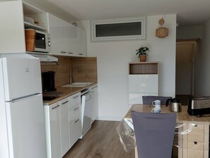 Eine kleine Küche mit weißen Schränken, einem eingebauten Backofen, einer Spüle und einem Essbereich mit Tisch und Stühlen.