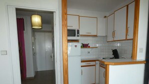 Una cocina compacta con armarios blancos, un microondas, un refrigerador y un lavamanos.