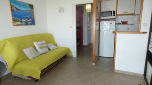Una habitación con un sofá amarillo, una cocina con armarios blancos, un microondas y un refrigerador.