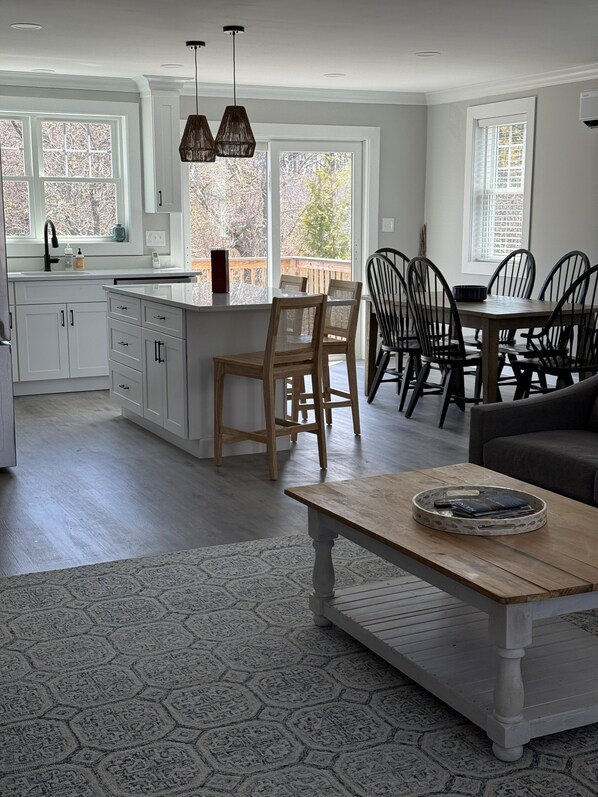 A spacious kitchen with white cabinetry, a central island, and a dining area with wooden chairs. - New build. 3 bedroom Townhouse walking distance to York Beaches. (York)