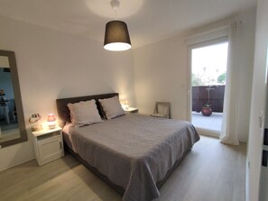 A bedroom with a bed, bedside lamps, a nightstand, a window with curtains, and a view of the outside. - Air-conditioned apartment in CAP D'AGDE - 2/4 guests (Cap d'Agde)