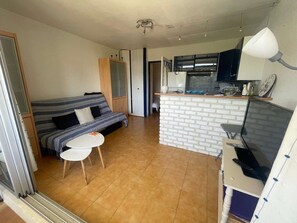Un espace de vie compact comprenant un canapé, une petite table, un coin cuisine avec un réfrigérateur et un téléviseur.