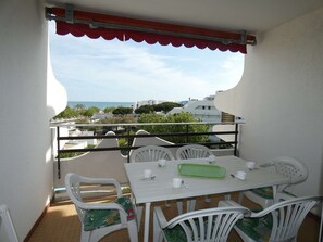 Un balcón con mesa y sillas, vista al mar y edificios al fondo.
