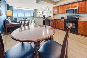 A modern kitchen with wooden cabinets, a microwave, an oven, and a dining area with a round table and chairs. - Amazing Water Park & Amazing View at Dunes Village (Myrtle Beach)