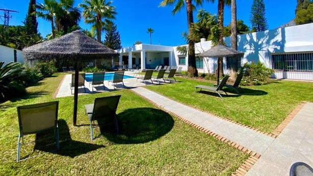 A pool area with lounge chairs, a thatched-roof structure, and palm trees. - Large villa Puerto Banús 10 bedrooms with pool and jacuzzi (Marbella)
