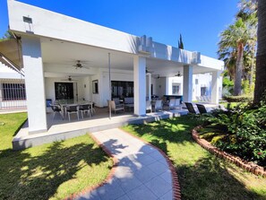 Une maison moderne dotée d’un patio couvert, d’un espace salon extérieur et d’un jardin.