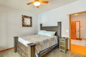 Un dormitorio con una cama de madera, una mesita de noche, un aparador, un ventilador de techo y una puerta que da a otra habitación.