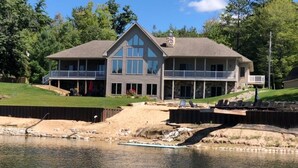 A large, two-story house with a balcony, situated next to a body of water.
