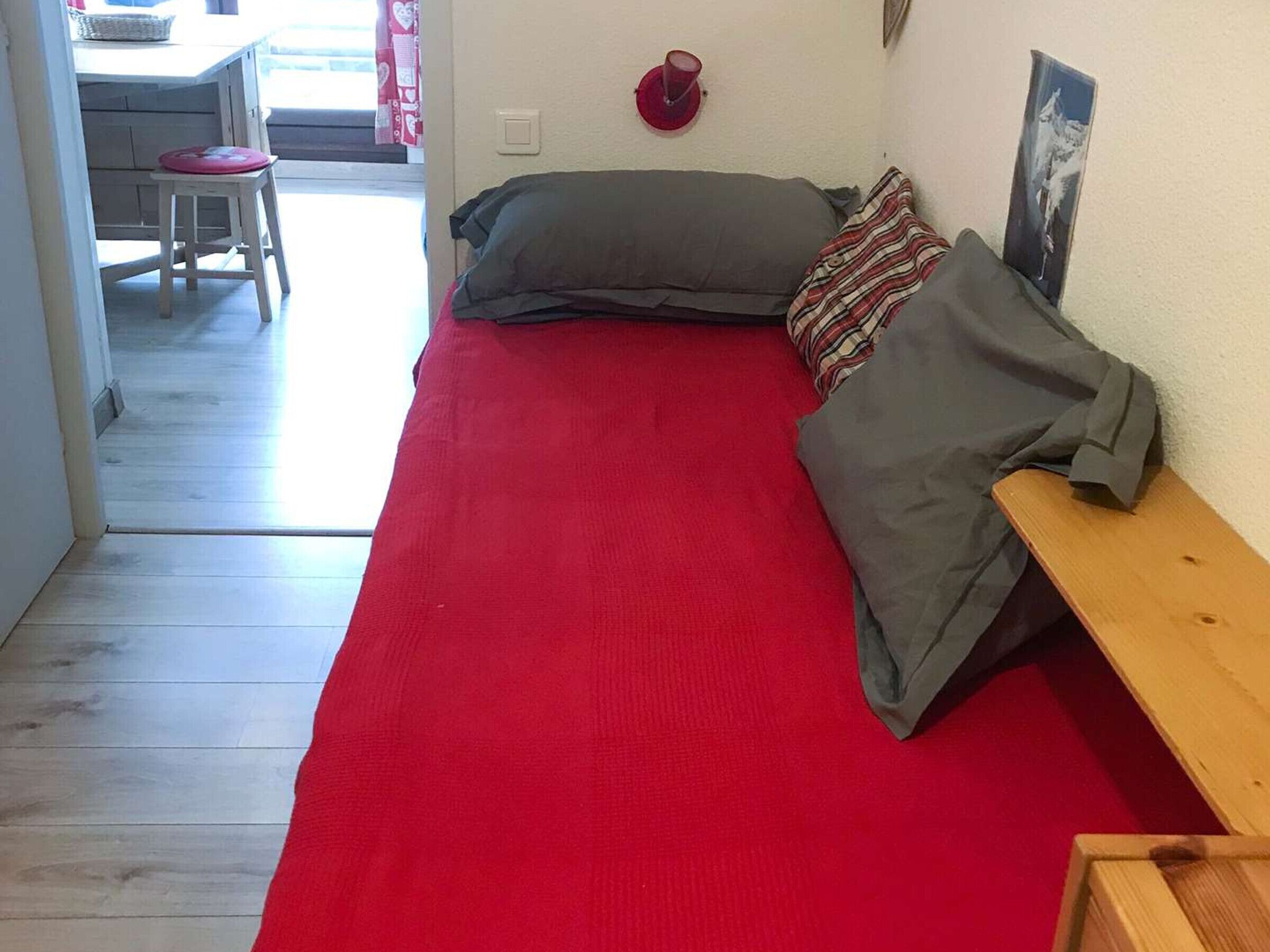 A room with a bed, a wooden bench, a red rug, a grey pillow, and a wall-mounted picture.