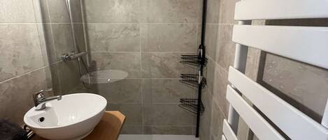Ein Badezimmer mit einem weißen Waschbecken, einer Dusche und einem Handtuchhalter.