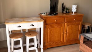 A compact kitchen with a wooden cabinet, two stools, a small table, and a television. - Cozy duplex near the sea - 4 guests (Merville-Franceville-Plage)