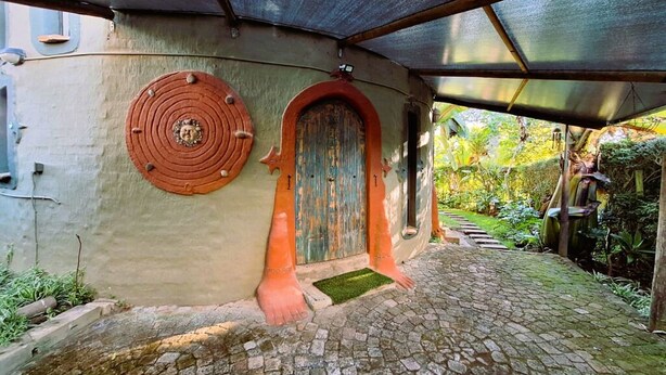 Un bâtiment doté d’une porte circulaire et d’une porte rectangulaire, toutes deux munies de poignées en métal, d’un chemin pavé et d’une zone abritée surmontée d’un toit en métal.