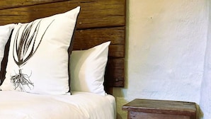 Un lit avec une literie blanche et deux oreillers, dont l’un est orné d’un motif de feuilles, adossé à une tête de lit en bois et placé devant un mur uni.