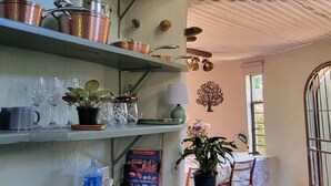 Une cuisine avec des étagères où sont rangées des casseroles en cuivre, une table ornée d’une plante en pot et une fenêtre offrant une vue agréable.