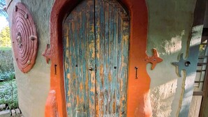 Une porte en bois rustique, dont la texture est marquée par les intempéries, est encadrée par une arche et flanquée d’éléments décoratifs sur le mur.