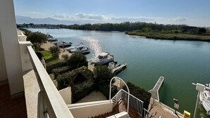 Uitzicht op een rivier vanaf een balkon, met stilgelegde boten, een heldere lucht en een bergketen in de verte.