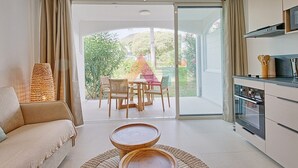 A modern kitchen with a dining area, a sofa, and a view of a garden through a glass door. - Studio suite in Anse Marcel - 2 guests (Saint-Martin)