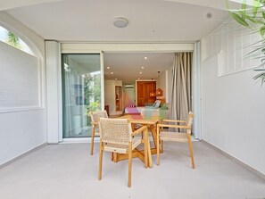 A dining area with a table and chairs, a sliding glass door, and a view into a room with a bed and curtains. - Studio suite in Anse Marcel - 2 guests (Saint-Martin)