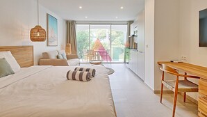 A modern bedroom with a large bed, a desk, and a view of a garden through a sliding door. - Studio suite in Anse Marcel - 2 guests (Saint-Martin)
