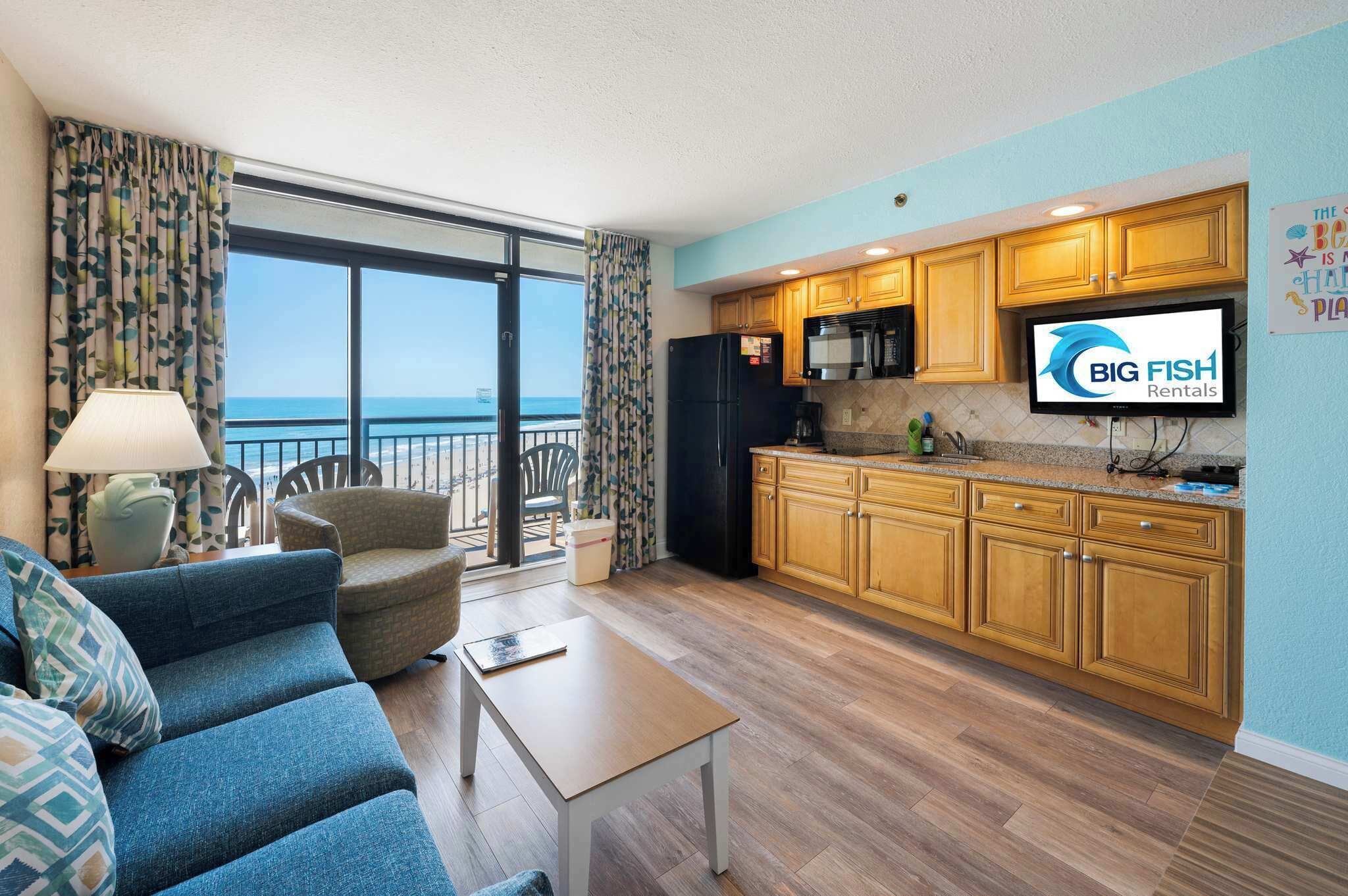 A living room with a sofa, a table, and a TV in a room with wooden cabinets and a view to the outside.