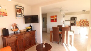A living room with a TV, wooden cabinet, and a dining area with wicker chairs. - Stunning AC Apartment for 6, Beach Access, Private Parking (Sète)
