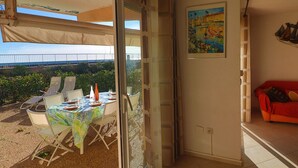 A room with a glass door leading to an outdoor area with a table and chairs, a red sofa, and a painting on the wall. - Stunning AC Apartment for 6, Beach Access, Private Parking (Sète)