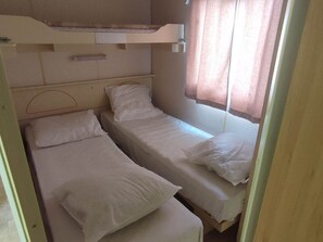 Een kleine kamer met twee eenpersoonsbedden, een stapelbed erboven en een raam met gordijnen.