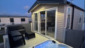 Een bubbelbad met LED-verlichting, een overdekt terras met zitplaatsen en een klein gebouw met glazen deuren.