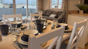Een eetruimte met een tafel gedekt voor vier personen, stoelen en uitzicht op de stad door grote ramen.