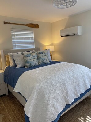 Ein Schlafzimmer mit einem Bett, einem Holzschläger, einem Fenster mit Jalousien, einer Wandklimaanlage und einer Nachttischlampe.
