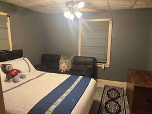Ein Schlafzimmer mit Bett, Deckenventilator, Fenster mit Jalousien, Nachttisch und Teppich.