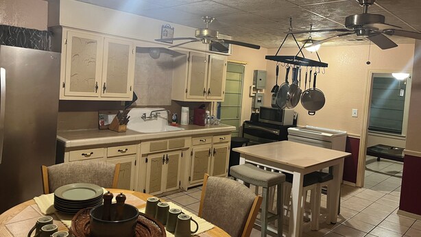 A kitchen with cabinets, a sink, a stove, a dining table with chairs, and ceiling fans. - 2-bedroom house in enchanting Bandera with cool AC breeze (Bandera)