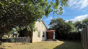 A residential backyard with a house, a wooden shed, a fenced area, and a tree. - 2-bedroom house in enchanting Bandera with cool AC breeze (Bandera)