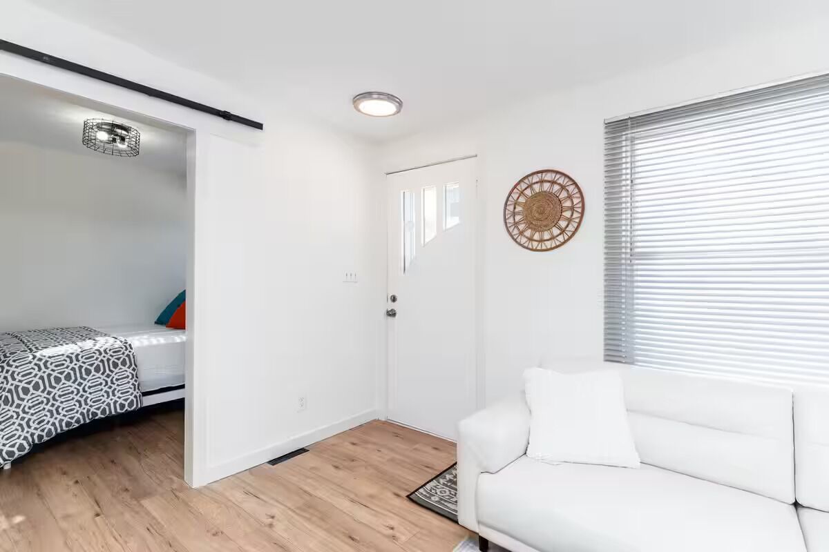 A modern room with a bed, a white sofa, a wooden floor, a ceiling light, and a door.