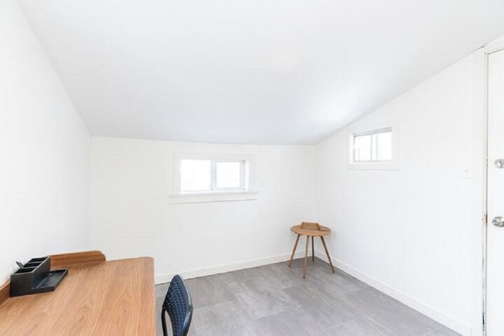 Una habitación con una mesa de madera, una silla, una mesita redonda y dos ventanas.