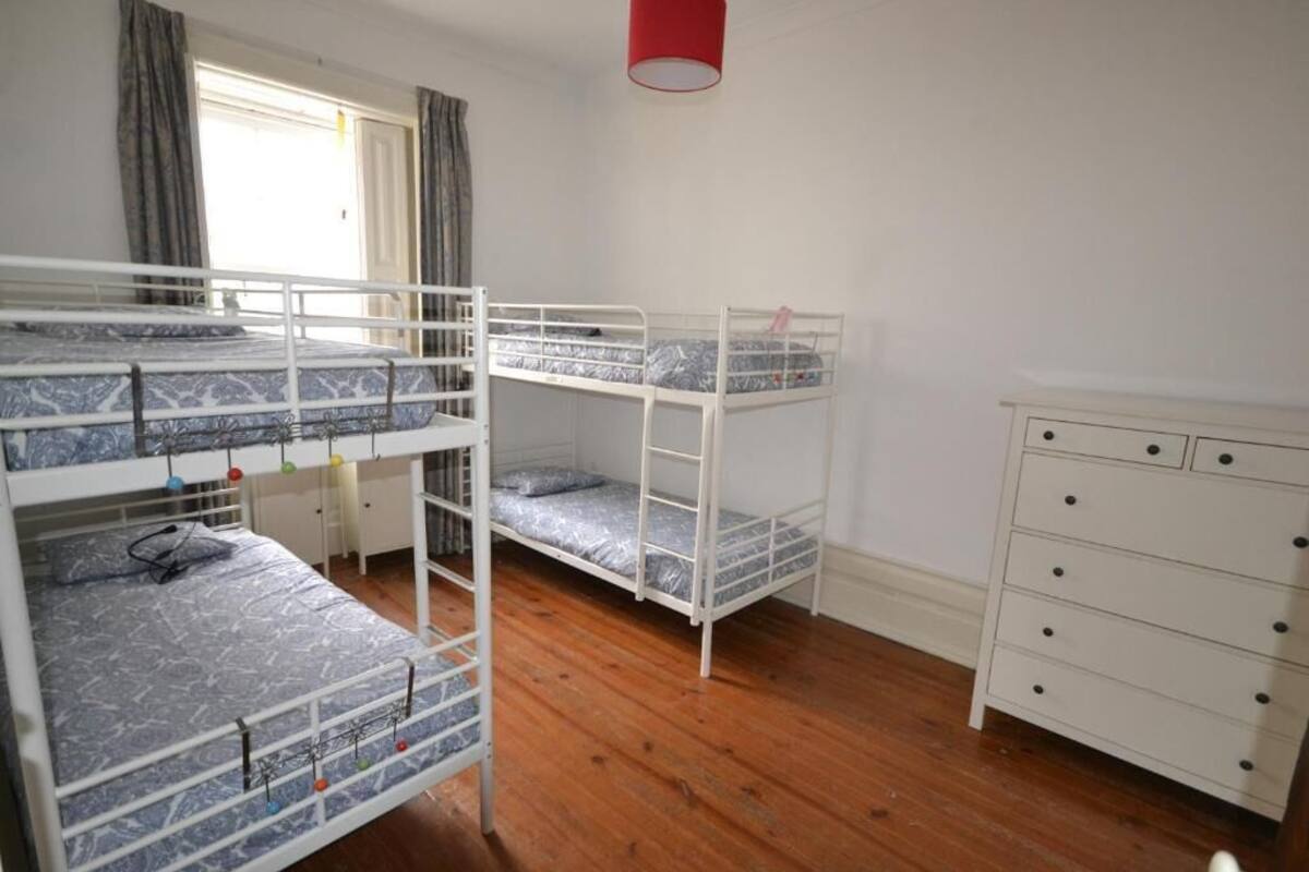 A room with bunk beds, a white dresser, and a window with curtains.