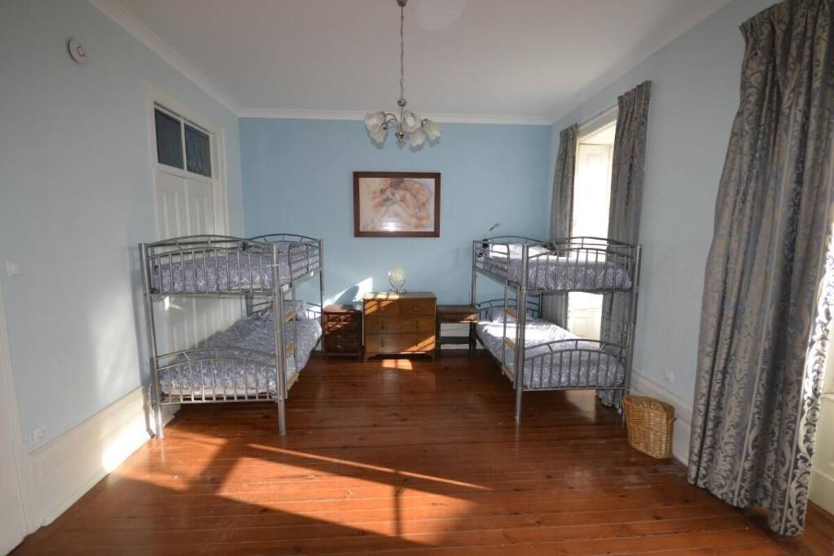 A room with bunk beds, a wooden floor, a chandelier, a framed picture on the wall, and a window with curtains.