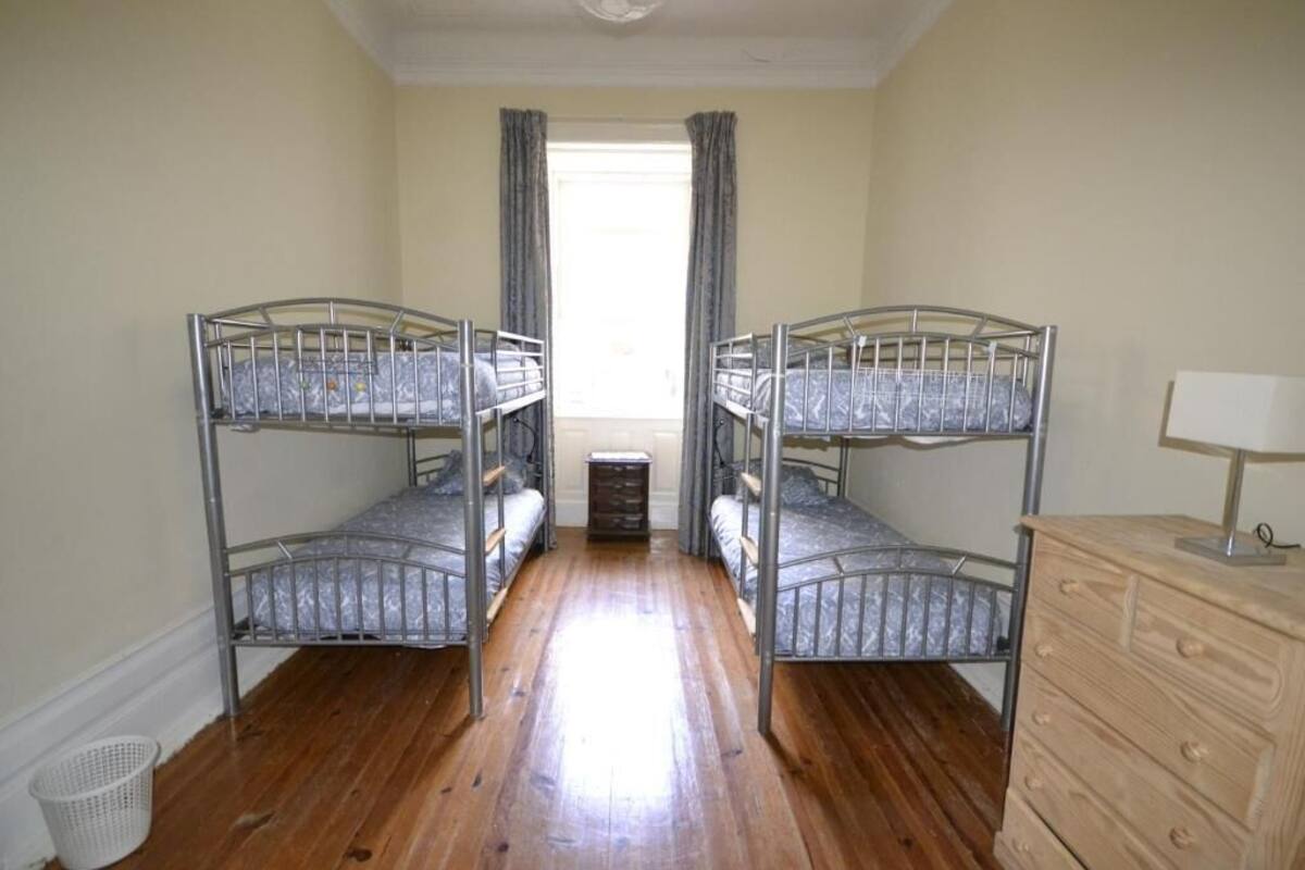 A room with two bunk beds, a wooden floor, a dresser, and a window with curtains.