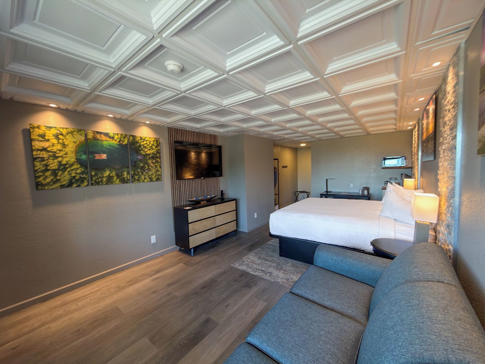 Una habitación de hotel moderna con una cama grande, un área de estar, un televisor de pantalla plana y un elemento decorativo en la pared.