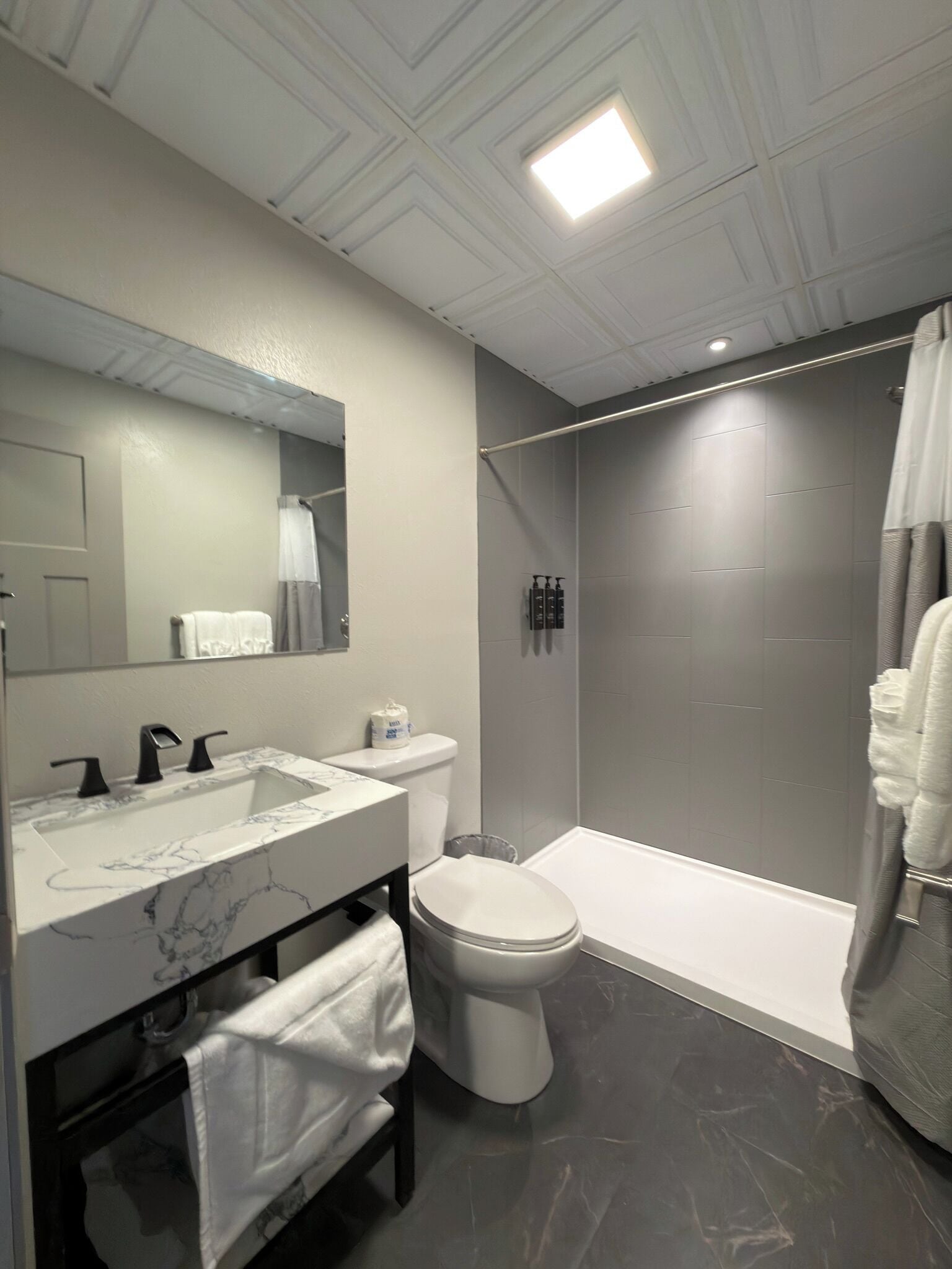 A modern bathroom with a marble sink, a toilet, a shower, and a large mirror.