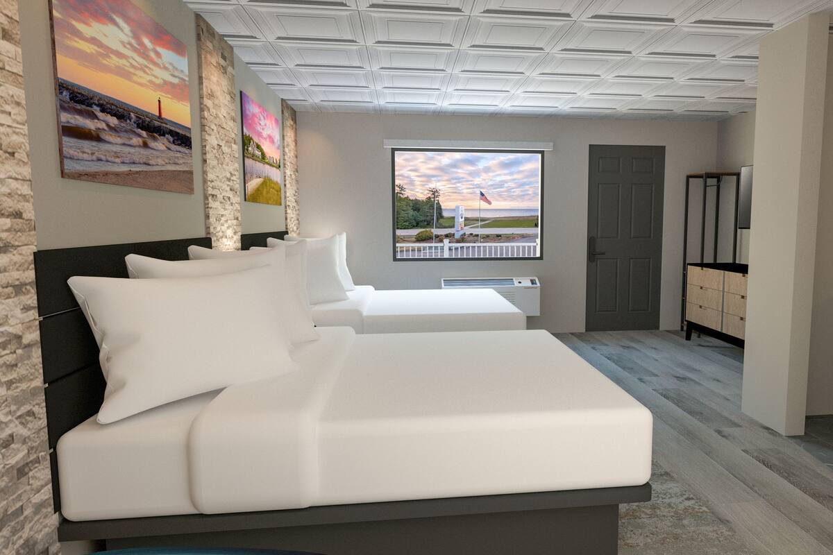 A bedroom with a large bed, a desk, a dresser, and a window with a view of the beach.