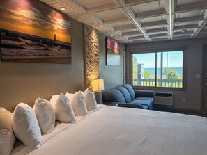 Una habitación de hotel con una cama grande, una zona de estar con vistas, una pared decorativa de piedra y un cuadro de un atardecer.